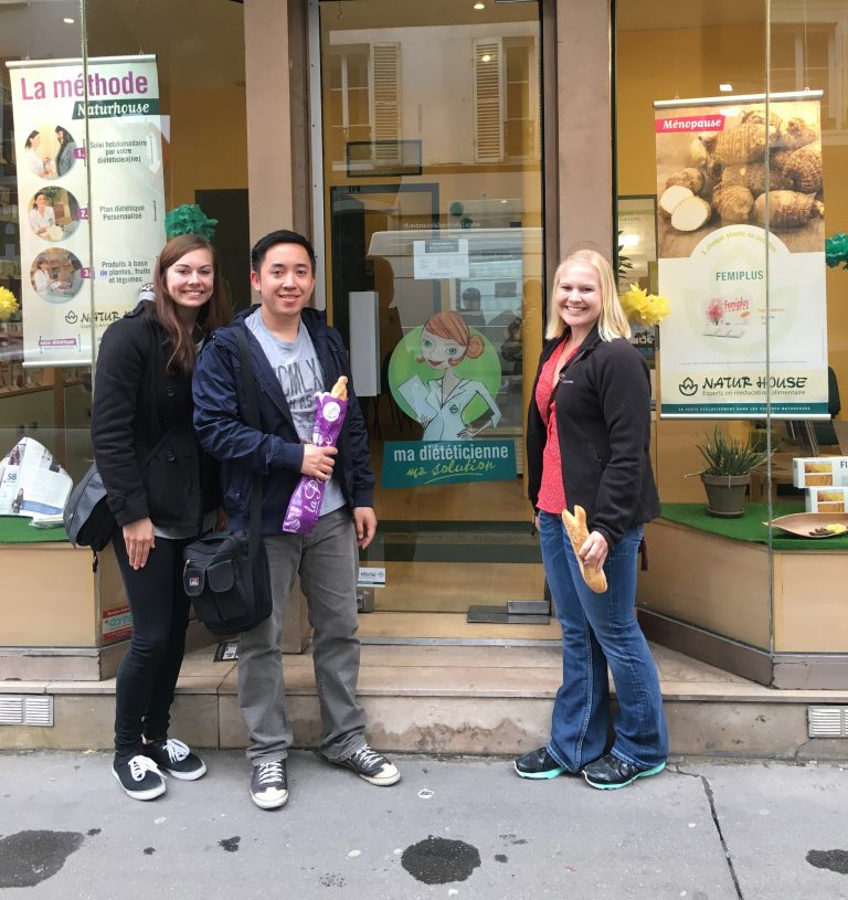 Three students in front of a french shop, the two women and three men are smiling at the camera.