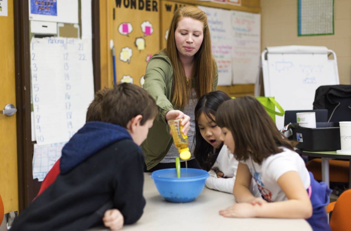 A dietetian shows students honey squeezing into a blue bowl as four small children surround the bowl and watch.